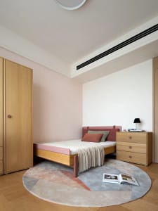 A well-lit bedroom with a wooden floor, a pink mattress, and a brown dresser, creating a comfortable atmosphere
