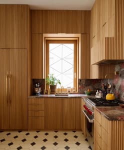 Warm kitchen with wooden cabinets, countertops, and various kitchen items, including bottles, cups, and an orange