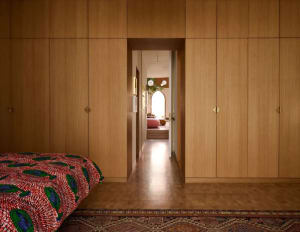 Cozy bedroom with wooden floors and walls, featuring a bed near the left wall, a chair near the right side, and a potted plant in the center