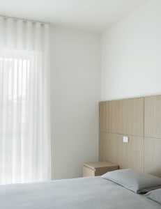 A clean and organized bedroom with two beds, a nightstand, and a wooden headboard, set against a white wall