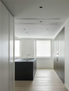 Modern kitchen with white cabinets, black countertops, and natural light from two windows, featuring a dining table and kitchen island