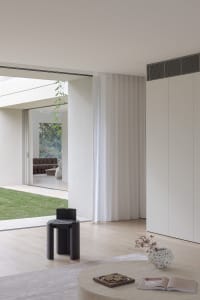 Open living area with white walls, wooden floors, and large windows, featuring a kitchen, dining room, and living room with couches, a chair, and a dining table
