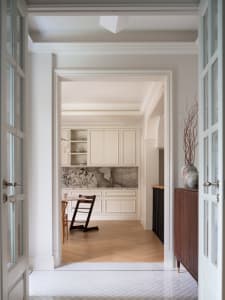 A clean and organized kitchen with white walls, wooden floors, and a dining table with various items on its surface