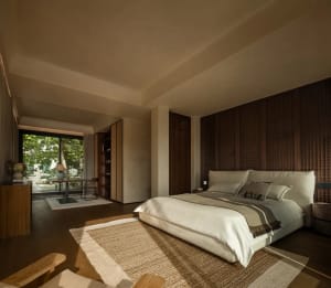 Cozy bedroom with a brown bed, two chairs, and a dining table on a hardwood floor, with a warm and inviting ambiance