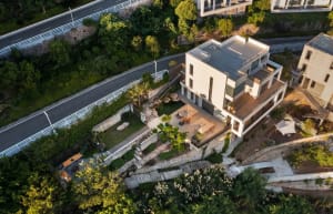 A modern house with a white and gray facade, situated on a hillside surrounded by trees, blending into the environment