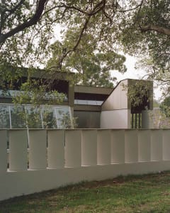 A modern house with a white exterior, surrounded by trees, featuring a large window and a well-maintained, well-lit atmosphere