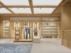 A modern retail space with a wooden floor, clothes hanging on the walls in organized sections, and soft diffused lighting creating a warm atmosphere