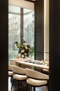 A dining room with a wooden table and chairs, a potted plant, and natural light from a window