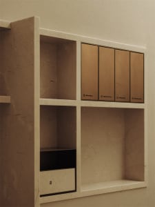 A room with a white marble wall and a white shelf featuring three gold boxes, creating a sophisticated atmosphere with a clean and elegant appearance