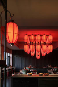 A modern restaurant with a red and black color scheme, featuring a dining area, bar, and dim lighting