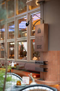 A modern restaurant with a large window, natural and artificial lighting, a dining table, chairs, cups, and bottles