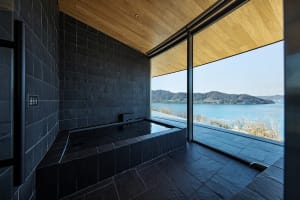 Bathroom with stone walls, a large window, a bathtub, sink, and toilet, in a modern and minimalistic style