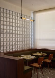 A cozy restaurant interior with a long wooden dining table and chairs, set with cups, bowls, and wine glasses, under warm lighting