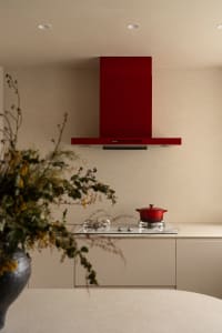 Modern kitchen with a red oven and cabinet, white countertops, and natural light from a window