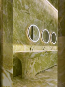 A well-lit bathroom with a green marble sink, a mirror above it, and three additional mirrors, creating a sense of luxury and sophistication