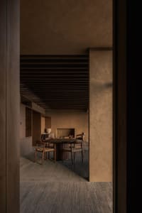 Cozy living room with a wooden floor, stone wall, and a dining table surrounded by chairs, lit by dim lighting