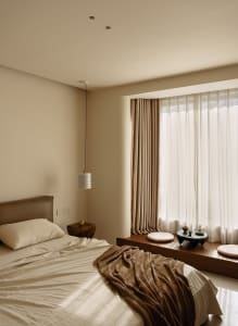 A well-lit bedroom with a bed, window, and table lamp, featuring wood and fabric materials in a warm and inviting space