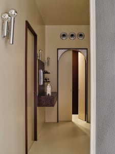 A modern bathroom with a sink, mirror, and door, featuring predominantly white surfaces and natural light