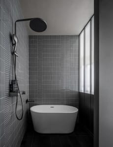 A dimly lit modern bathroom with a white bathtub, shower head, and tiled walls