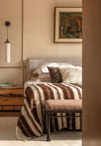 Cozy bedroom with a wooden floor, a brown color scheme, and dim lighting, featuring a bed, chair, and lamp