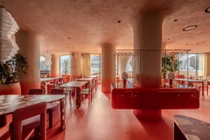 A modern restaurant with a red and white color scheme, featuring a large dining area with multiple tables and chairs, illuminated by natural light