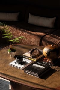 Cozy modern living space with a brown couch, a coffee table with books, a vase, and a bowl, and natural light from a window