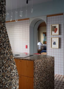 Modern kitchen with a marble countertop, sink under a cabinet, dining table, and chairs, with potted plants and natural light