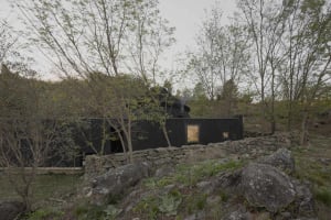 A serene outdoor scene of a rustic log cabin with a stone wall and chimney, set against a forest backdrop with natural sunlight