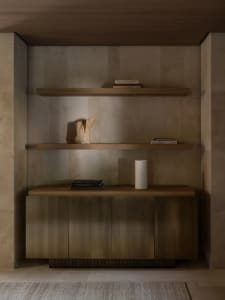 A cozy living space with a wooden bookshelf, books, and decorative items on a tiled floor, lit by soft warm light