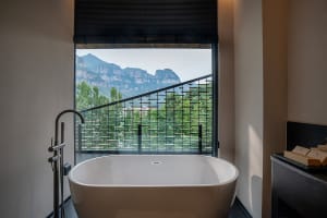 A serene bathroom with a white bathtub, black railing, and a large window offering a breathtaking mountain view