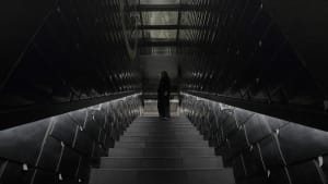 A black and white photograph of a stone staircase with a metal railing in a dimly lit area, captured from the bottom looking up