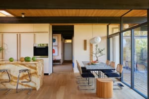 A modern kitchen with wooden floors and a dining table, featuring a center island with a sink and several chairs, well-lit with warm and inviting atmosphere