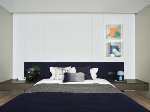 Cozy modern bedroom with a blue blanket, white walls, and natural light, featuring a bed, table, and vase