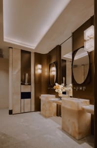 Modern bathroom with brown marble walls, a large mirror, a sink, and a toilet, with dim lighting creating a cozy atmosphere