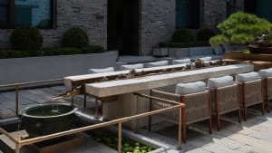 Outdoor patio with a stone table and metal railing, surrounded by comfortable seating and natural elements