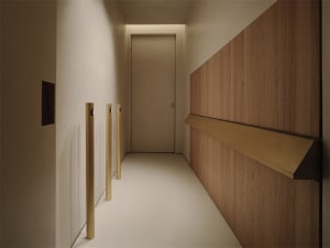 A calm and inviting hallway with a wooden floor and white walls, featuring a doorway and a wall-mounted light