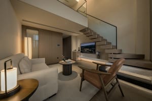 Comfortable living space with a wooden floor, a couch, a chair, and a television, lit by natural light from the windows