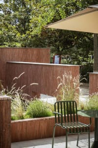 A modern outdoor dining space with a red brick wall, a green chair, and a dining table, surrounded by natural scenery and sunlight