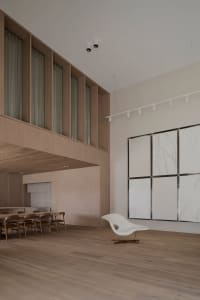 Modern living room with wooden floors, a white wall with a painting, a dining table, a couch, and natural light from windows