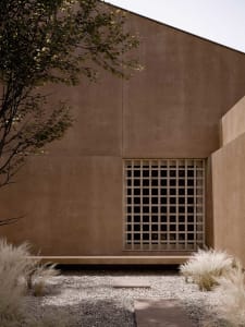 A modern building with a tan exterior and a large metal-framed window, set against a bright and sunny background