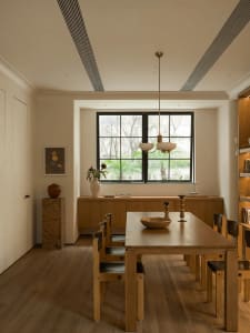 Warm and inviting kitchen with wooden floors and furniture, featuring a dining table, sink, and window, with a cozy atmosphere created by a bowl and vase on the table