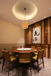 A dining room with a wooden table and chairs, set with various items, surrounded by warm wooden elements and natural light