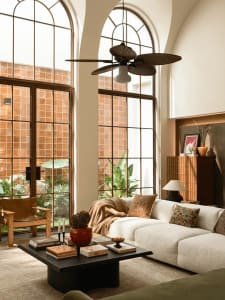 A well-lit living room with a white couch, chair, and dining table, surrounded by furniture and a large fan, creating a comfortable and inviting atmosphere