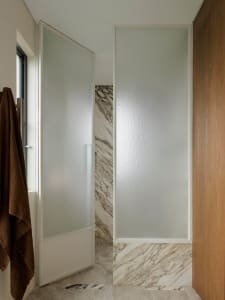 Bathroom with a marble-like shower stall, glass enclosure, and natural light from a window