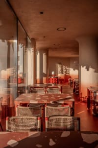 A dimly lit restaurant interior with red furniture, potted plants, and modern decor