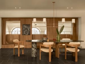 A modern dining room with a large wooden table and chairs, decorated with a bowl, vase, and potted plant, surrounded by natural light from the windows