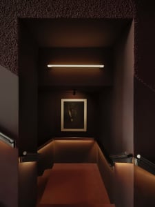 A dimly lit stairwell with a worn wooden staircase and red carpet, captured in black and white