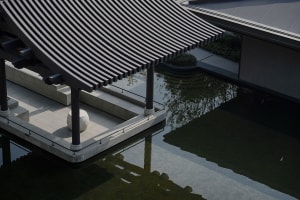 Photograph of a building with a black roof and white wall, situated near a body of water