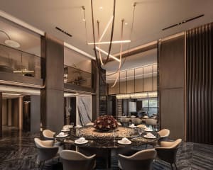 A modern dining room with a round table, chairs, wine glasses, and vases, lit by a chandelier and natural light