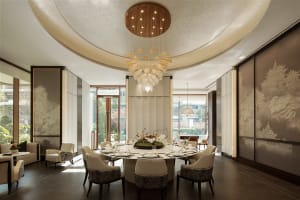 A well-lit dining room with a modern, spacious atmosphere, featuring a circular dining table, chairs, and a large chandelier